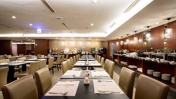 A spacious hotel dining area with multiple tables set for meals, a buffet line, and a well-lit ceiling with recessed lighting.