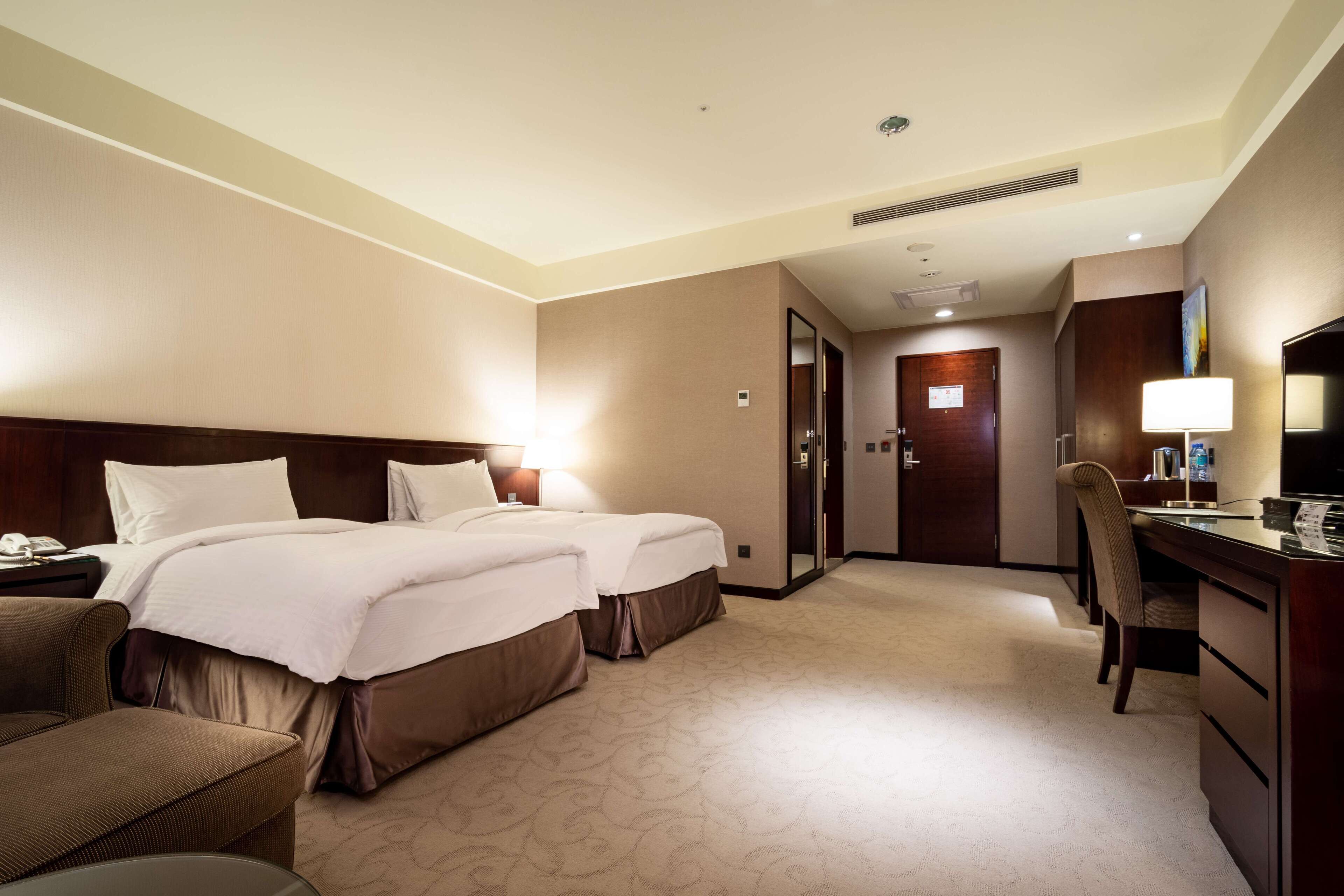 A hotel room with two beds, a desk, a chair, and a television.