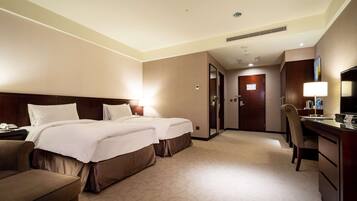 A hotel room with two beds, a desk, a chair, and a television.