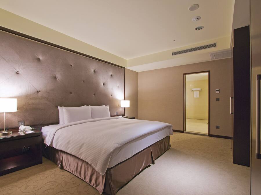 A hotel room with a large bed, two bedside tables with lamps, a wardrobe, and a bathroom visible through an open door.