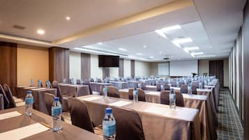 A conference room with long tables, water bottles, and a projector screen.
