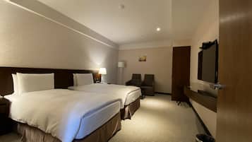 A hotel room with two beds, a desk, a chair, a TV, and a trash can.