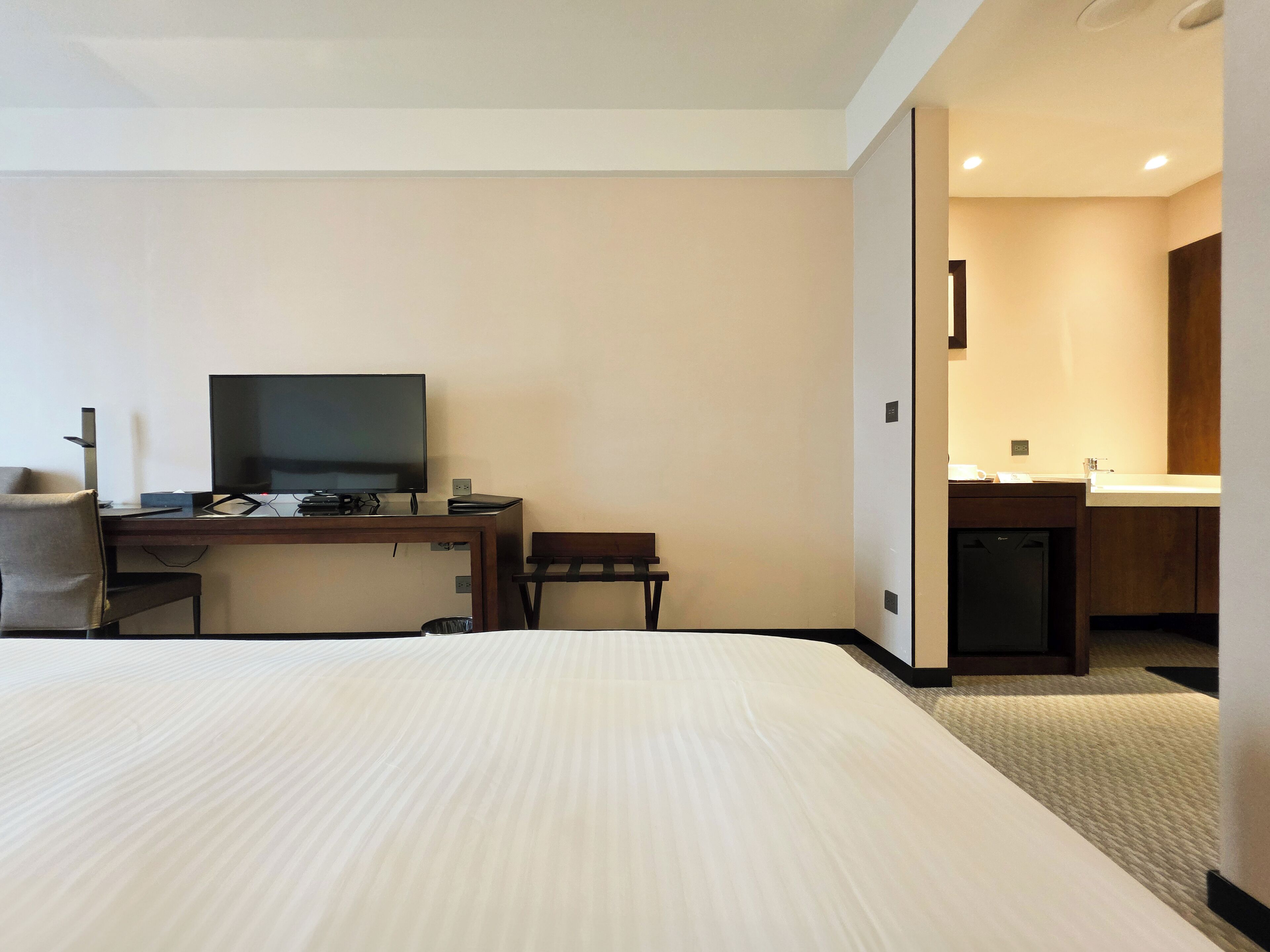 Una habitación de hotel con cama, escritorio con televisor, silla y una pequeña cocina.