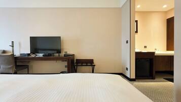 Una habitación de hotel con cama, escritorio con televisor, silla y una pequeña cocina.