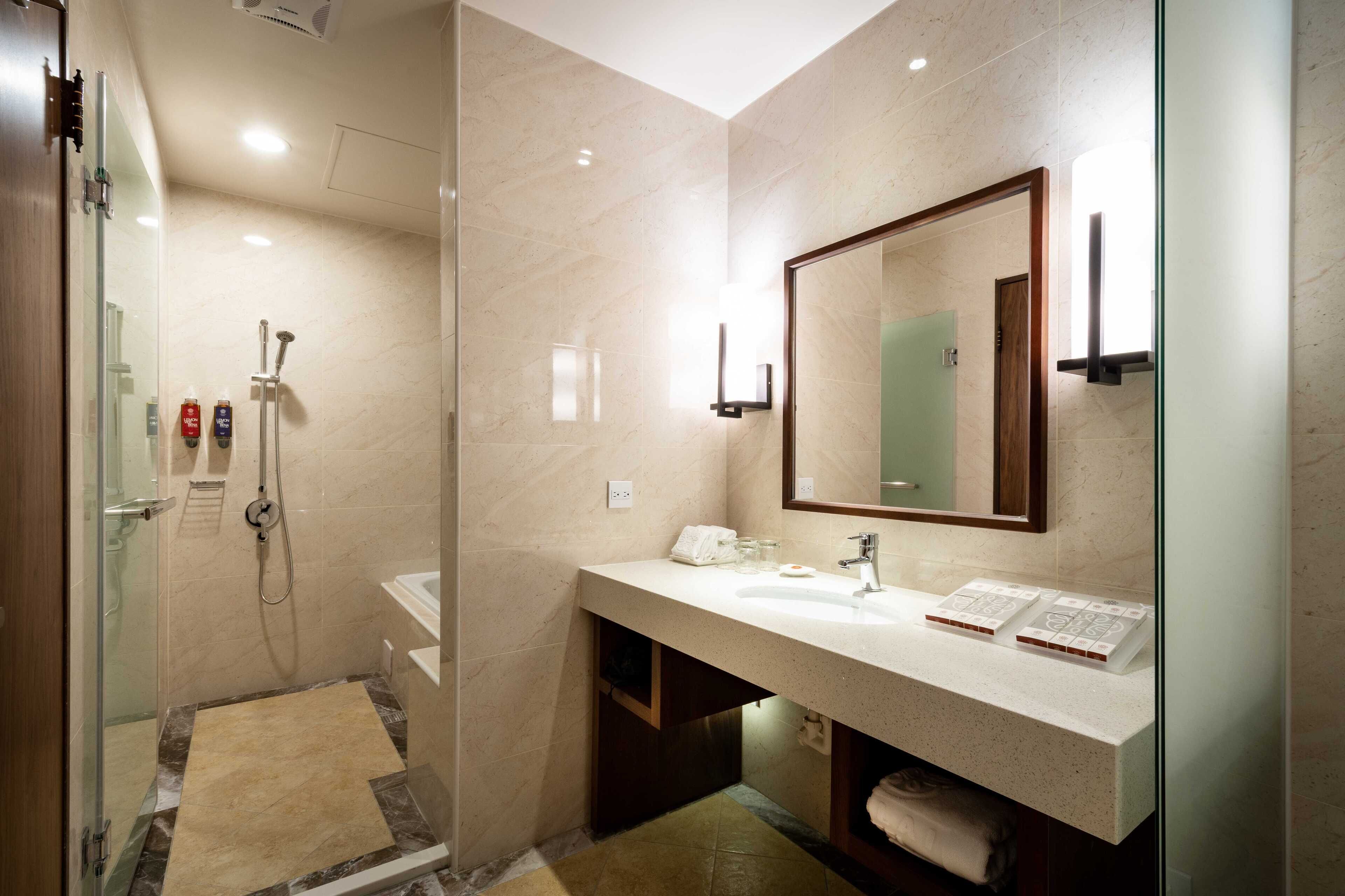 Un baño moderno con ducha envuelta en vidrio, lavabo con espejo y tocador con toallero.