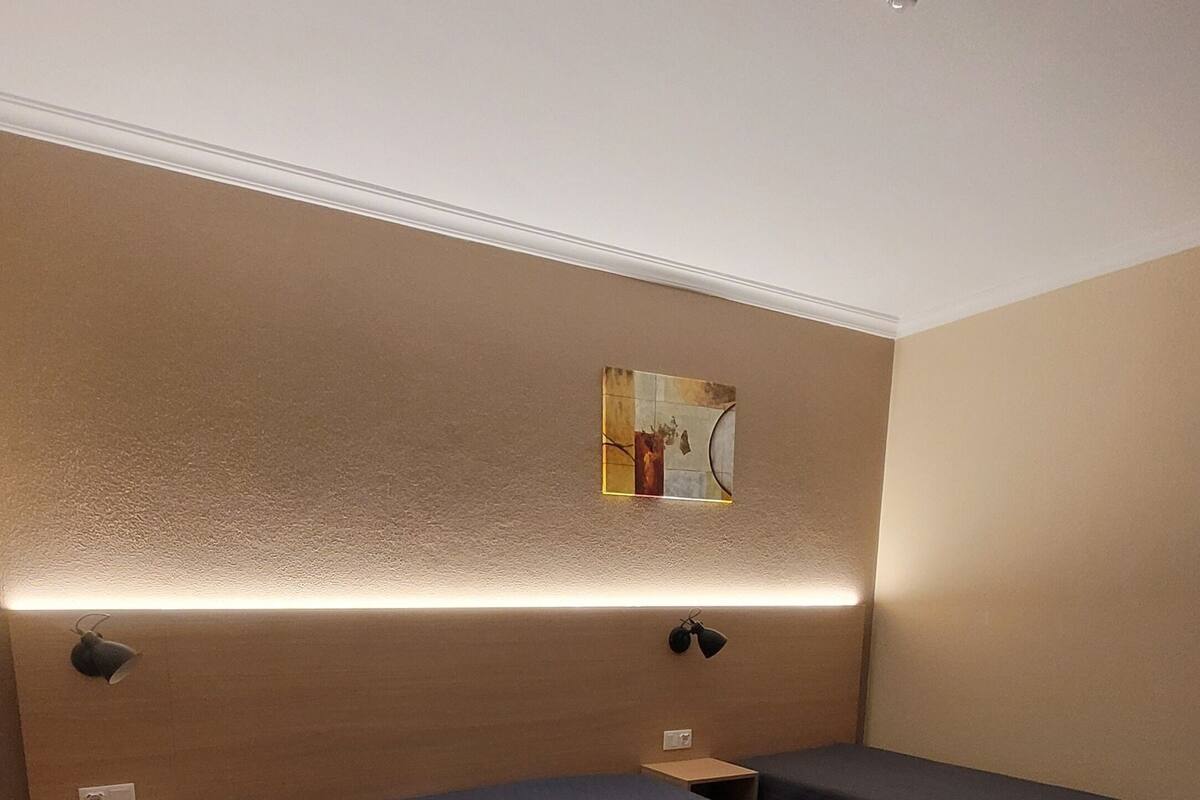 Habitación de hotel con dos camas, una lámpara de pared y una mesita.