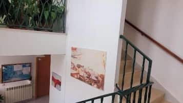 Una escalera con barandilla de metal, una pared con espejo y una planta visible a través de una malla de alambre.