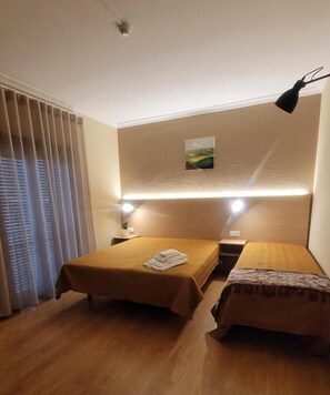 A hotel room with two beds, a nightstand, a lamp, and a painting on the wall.