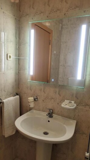 A bathroom with a sink, mirror, towel rack, and a small shelf.