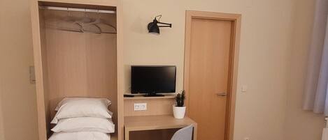 A bedroom with two beds, a desk with a computer, a chair, a wardrobe, and a door.