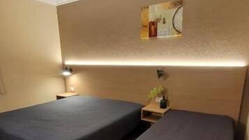 Una habitación con dos camas, un estante en la pared con una planta y un cuadro.