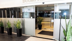 A hotel entrance with a modern design, featuring a glass door and a wooden mat at the entrance. There are potted plants placed outside the entrance. -  Duomi Hotel Buenos Aires (Buenos Aires)