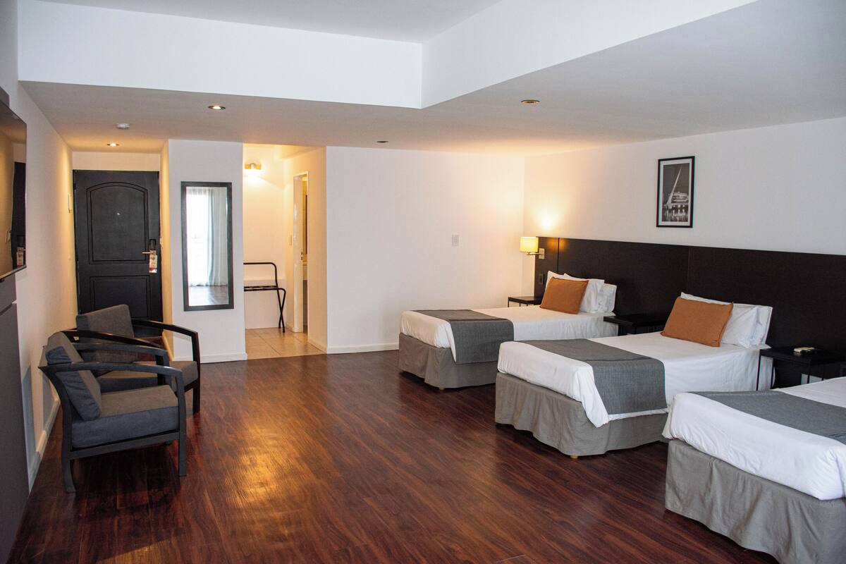 Une chambre d’hôtel avec quatre lits, un bureau, une chaise et une porte.