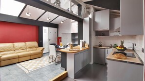 A modern kitchen with a central island, a dining area with a sofa, and a red accent wall. - Apartamentos El Tiempo (Madrid)