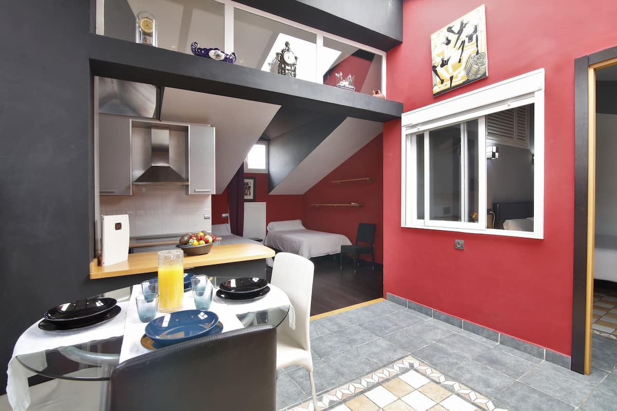 Een kleine keuken met een eethoek, een rode wand en een raam.