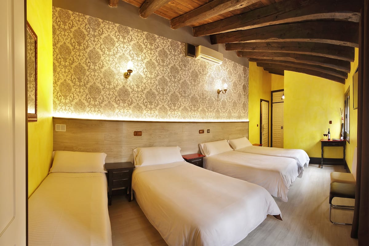 Een hotelkamer met twee bedden, houten balken in het plafond en behang met een patroon aan de muur.