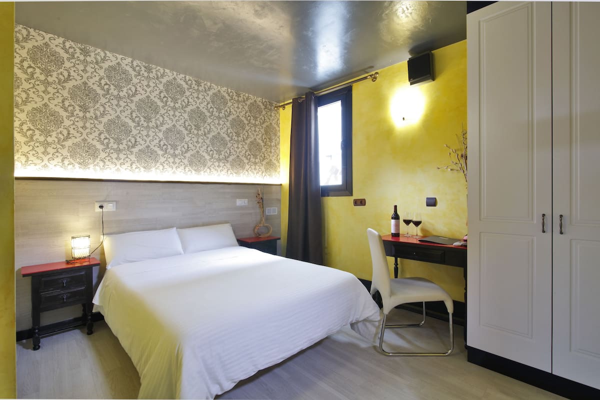 Een hotelkamer met een bed, een bureau met stoel, een kledingkast en een raam met gordijnen.