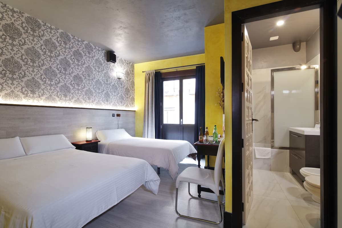 Een hotelkamer met twee bedden, een bureau met stoel, een badkamer met toilet en wastafel, en een kamer met een patroon op de muur.