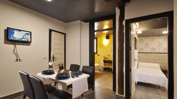 Hotelkamer met een bed, een zithoek met een tafel en stoelen, een aan de muur bevestigde televisie en een badkamer zichtbaar door een geopende deur.