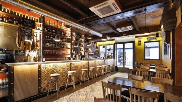 A bar with a long counter, stools, and a patterned floor. - Apartamentos El Tiempo (Madrid)