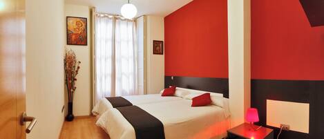Una habitació d'hotel moderna amb un llit gran, una taula de nit amb una làmpada i una paret d'accent vermella.