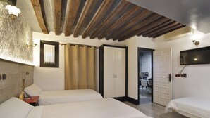 A room with two beds, a wooden ceiling, a TV mounted on the wall, and a door leading to another room. - Apartamentos El Tiempo (Madrid)