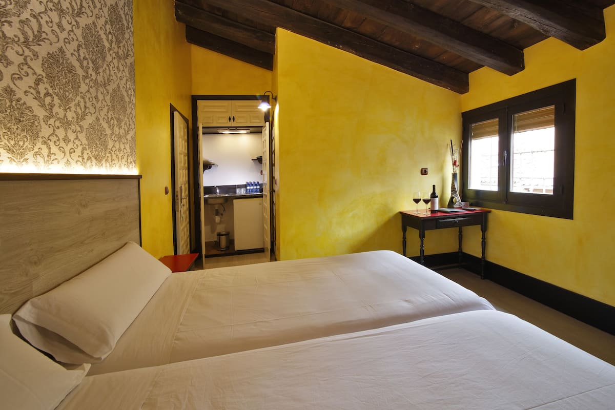 Een slaapkamer met een bed, nachtkastje, raam en een keuken op de achtergrond.
