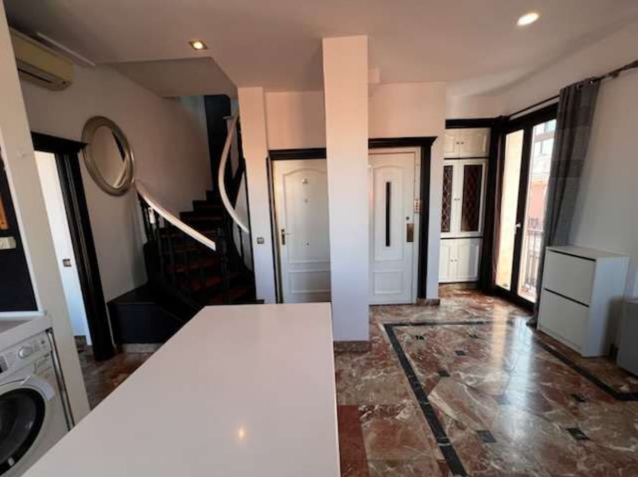Une cuisine spacieuse dotée d’un sol en marbre, d’un îlot central et d’un escalier menant à un autre niveau.