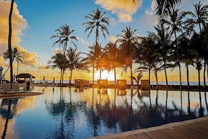 A poolside area with lounge chairs and a wooden deck, overlooking a sunset and palm trees. - Jatiúca Suítes Resort by Slaviero Hotéis (Maceió)