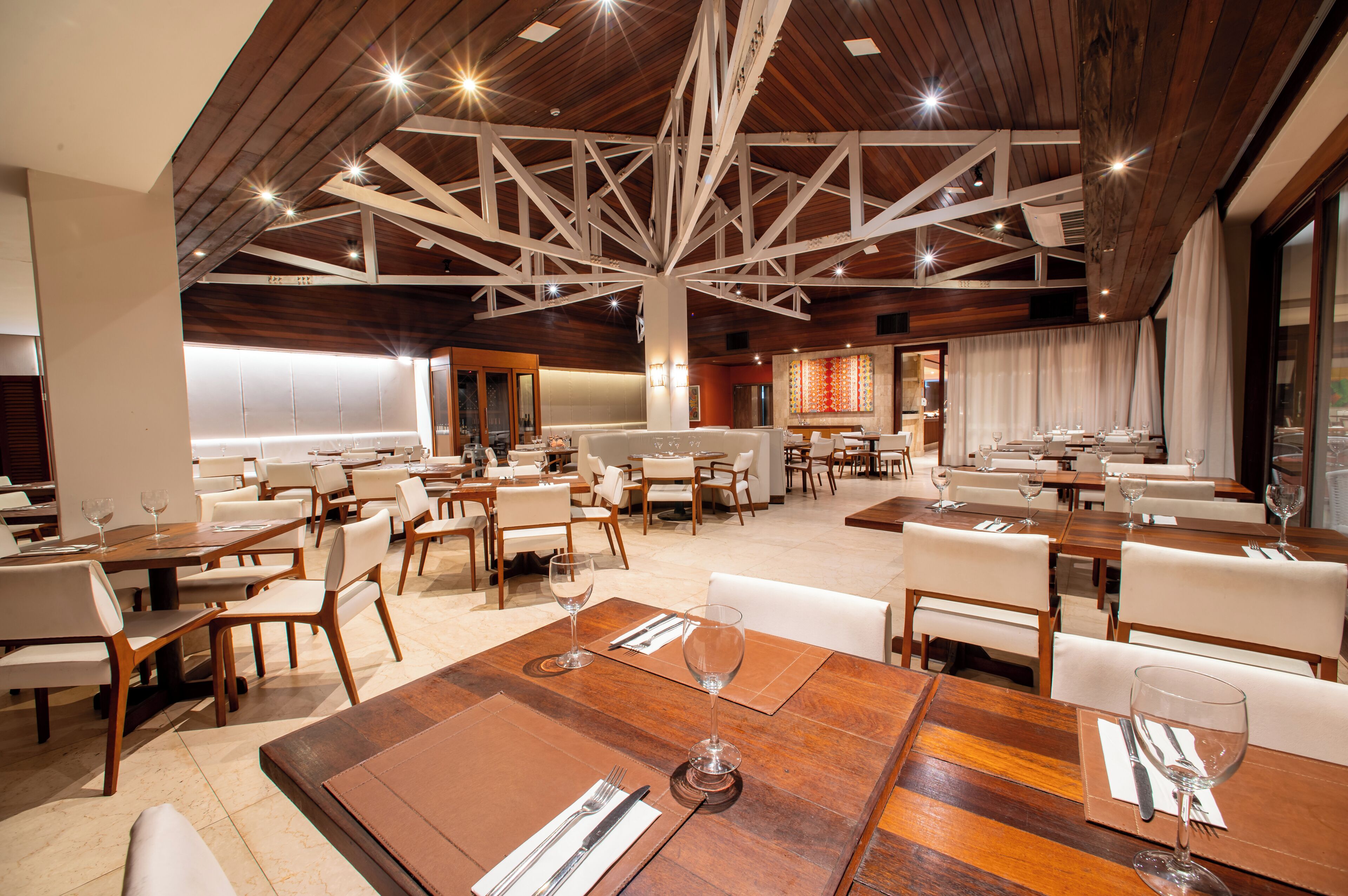Un restaurant spacieux avec des tables en bois et des chaises blanches, un plafond haut avec des poutres apparentes et un aménagement intérieur moderne.