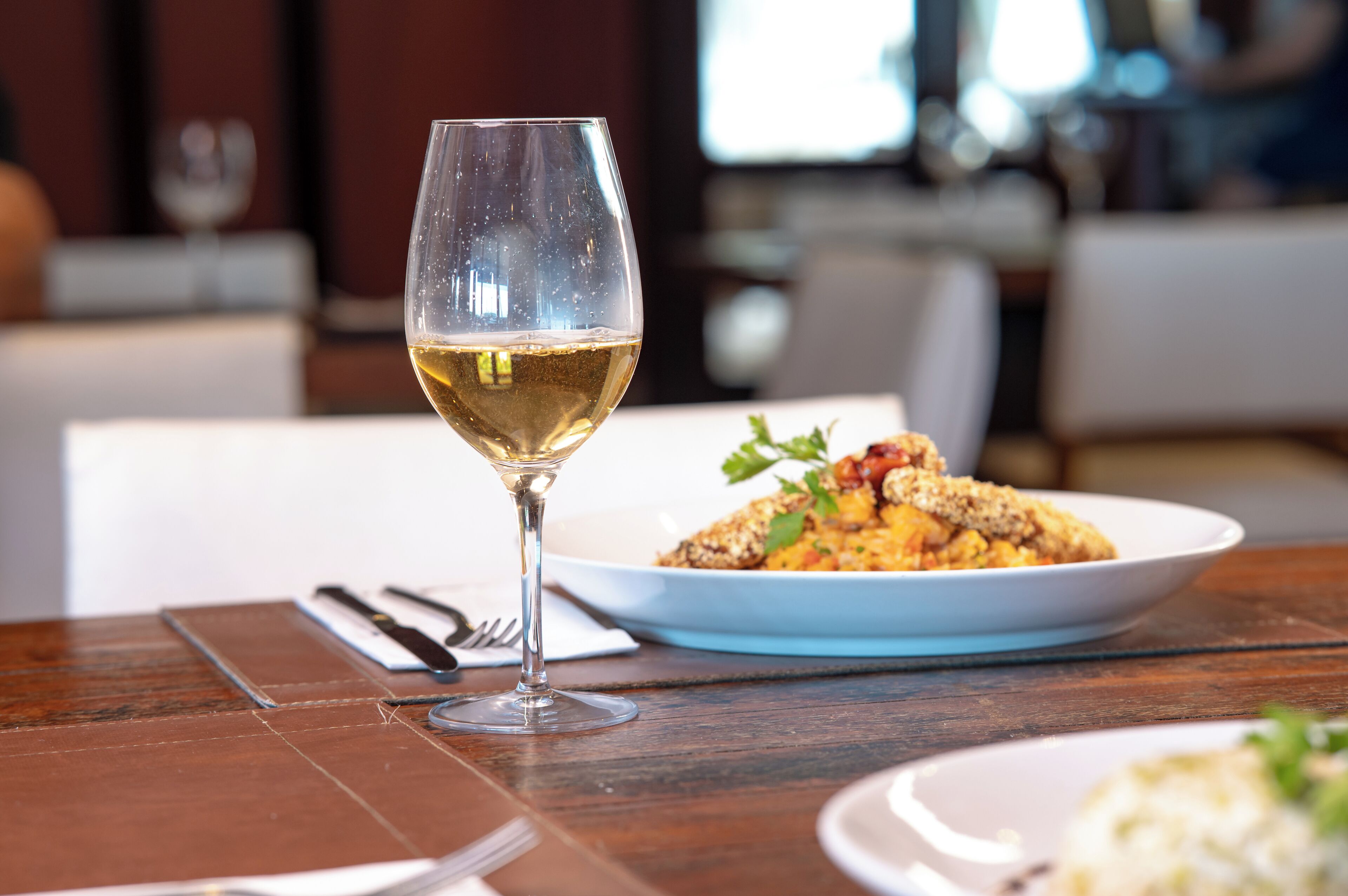 Una mesa de comedor con una copa de vino blanco, un plato de comida y un tenedor.