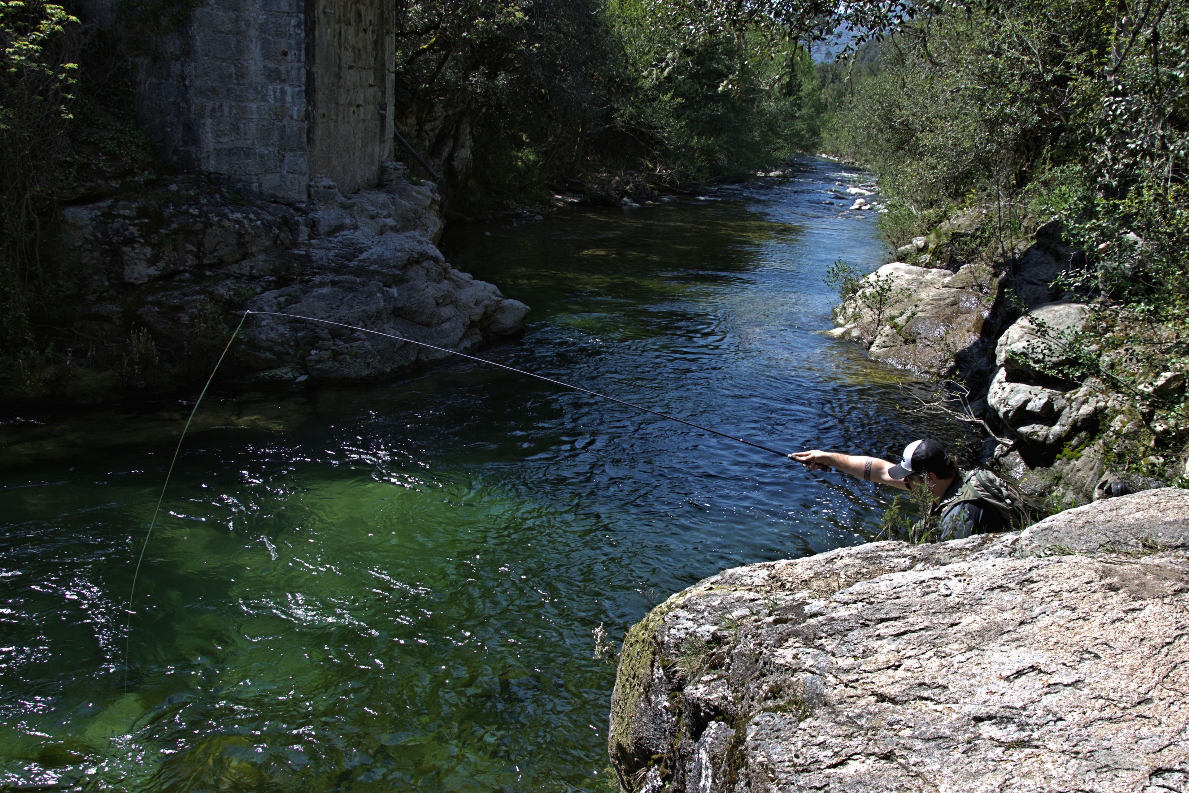 A river with clear water, surrounded by rocky terrain and dense vegetation.