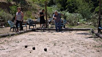 A group of people playing a game with balls on a gravel surface, surrounded by trees and greenery.