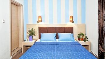 Quarto com parede listrada, duas luminárias de cabeceira, cama com roupa de cama azul e duas plantas em vasos.