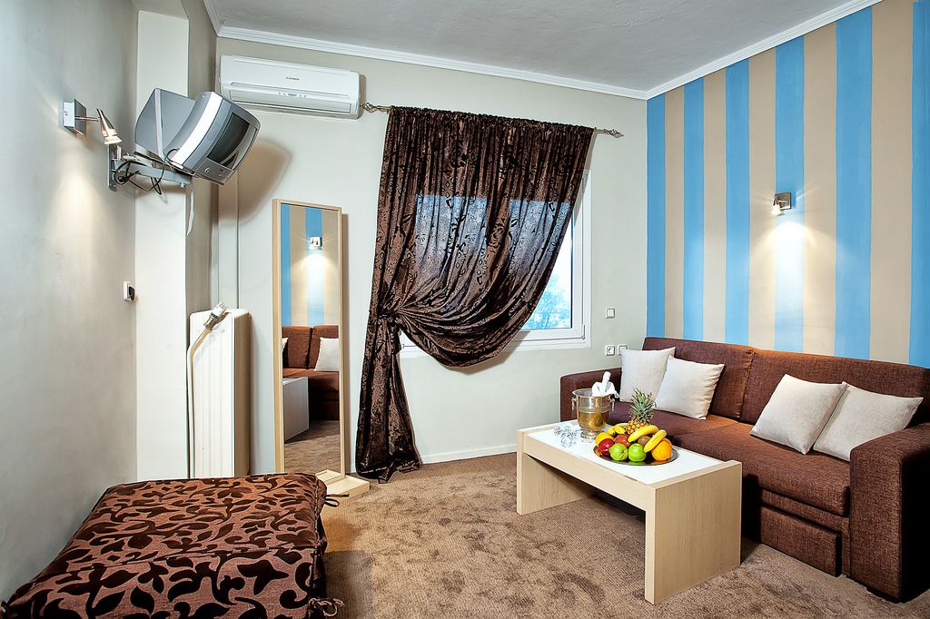 Ein gemütliches Hotelzimmer mit einer Sitzecke, einem kleinen Tisch mit Obst, einem Spiegel und einem an der Wand befestigten Fernseher.
