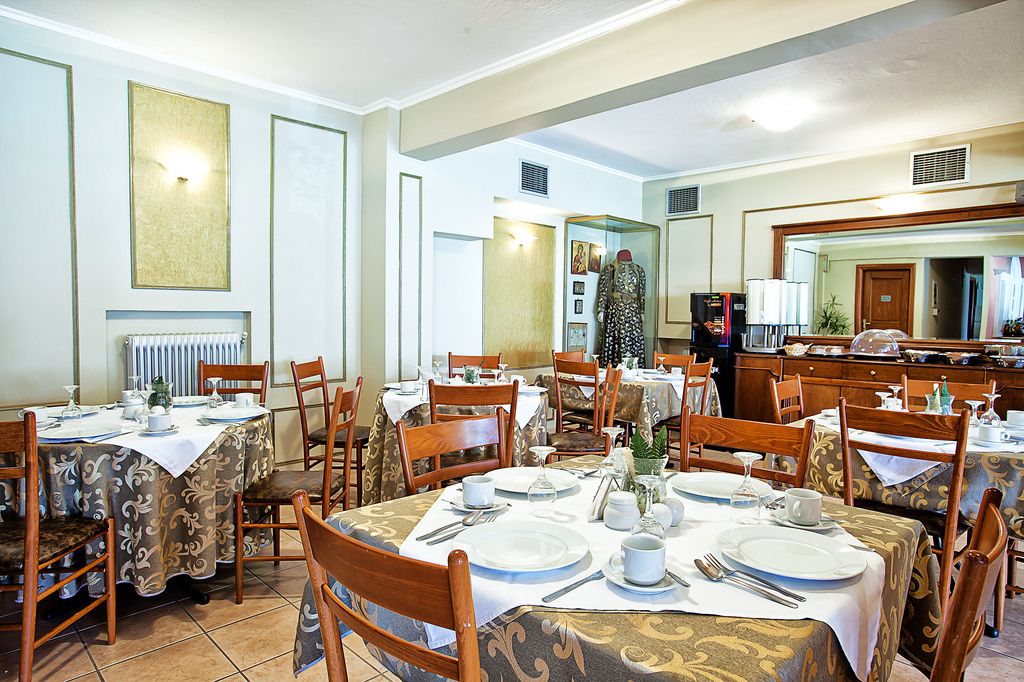 Un espace repas avec plusieurs tables dressées pour les repas, des chaises en bois et un grand miroir au mur.