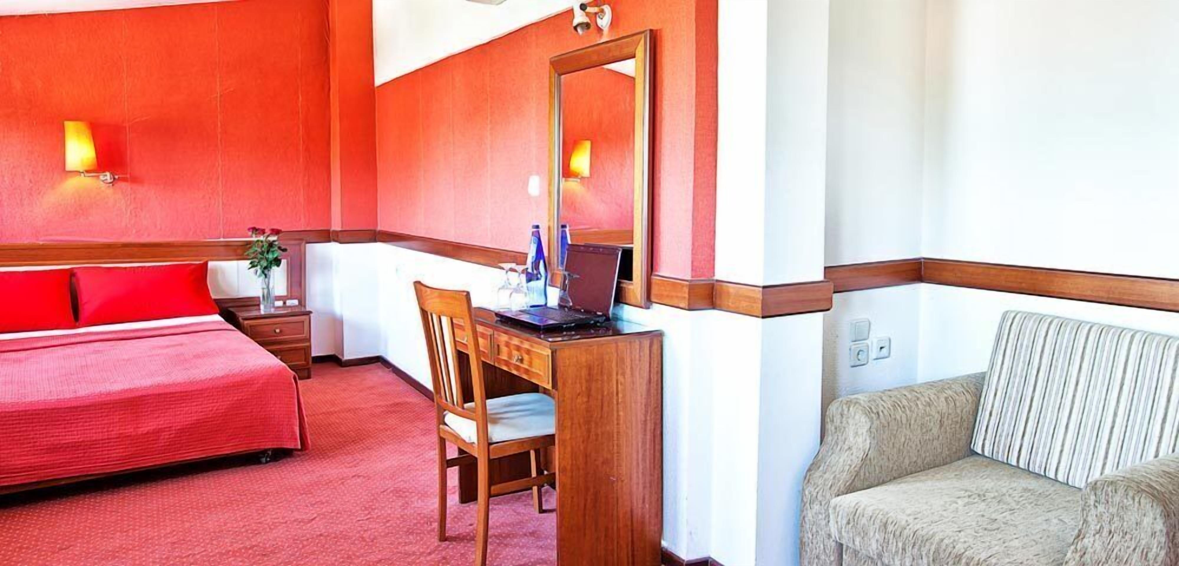 A hotel room with a bed, a desk with a laptop, a chair, and a sofa.