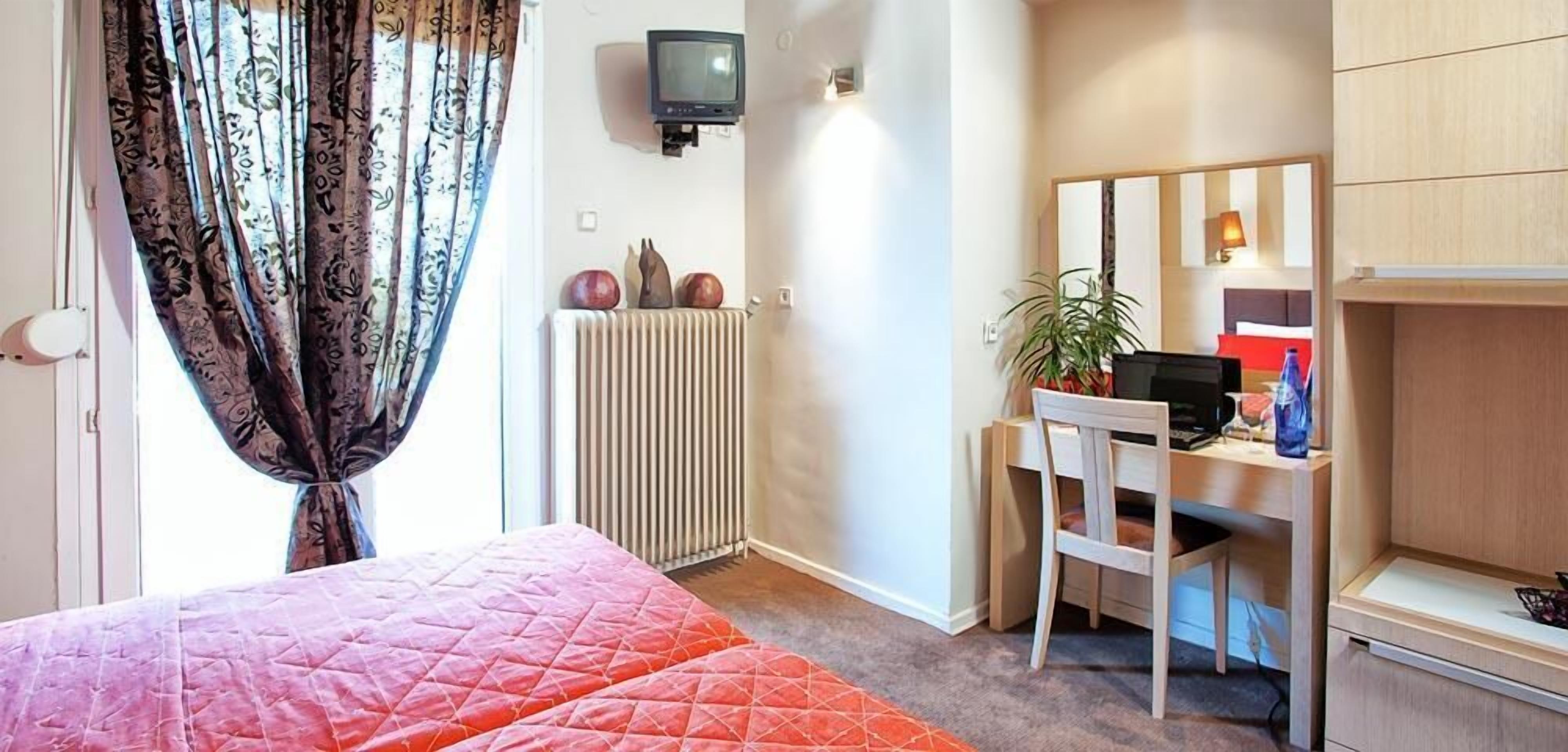 A bedroom with a bed, a desk, a chair, a radiator, a television, and a mirror.