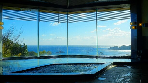 A modern indoor swimming pool with large windows offering a view of the ocean and distant land. - Shimoda View Hotel (Shimoda)