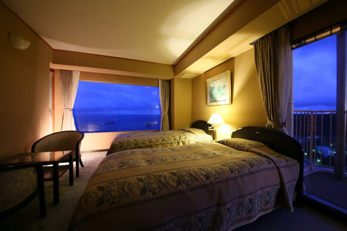 Habitación de hotel con dos camas, un escritorio y una silla. Amplia ventana con vista al mar.