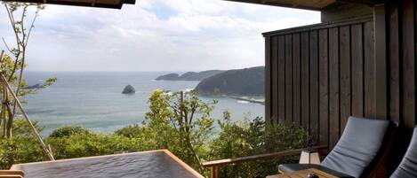 A wooden deck with a hot tub, seating area, and a view of the ocean.