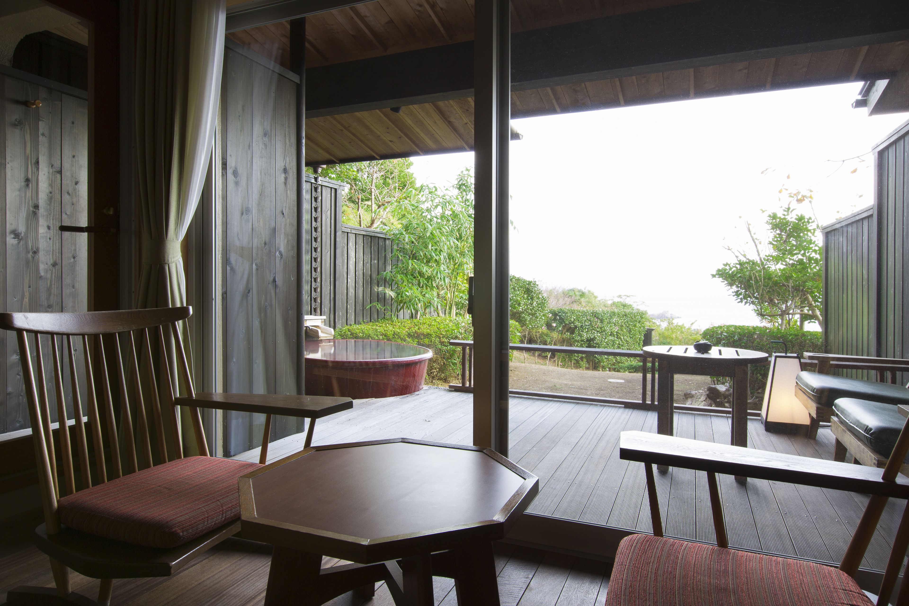 A wooden deck with a table and chairs, a hot tub, and a view of greenery.
