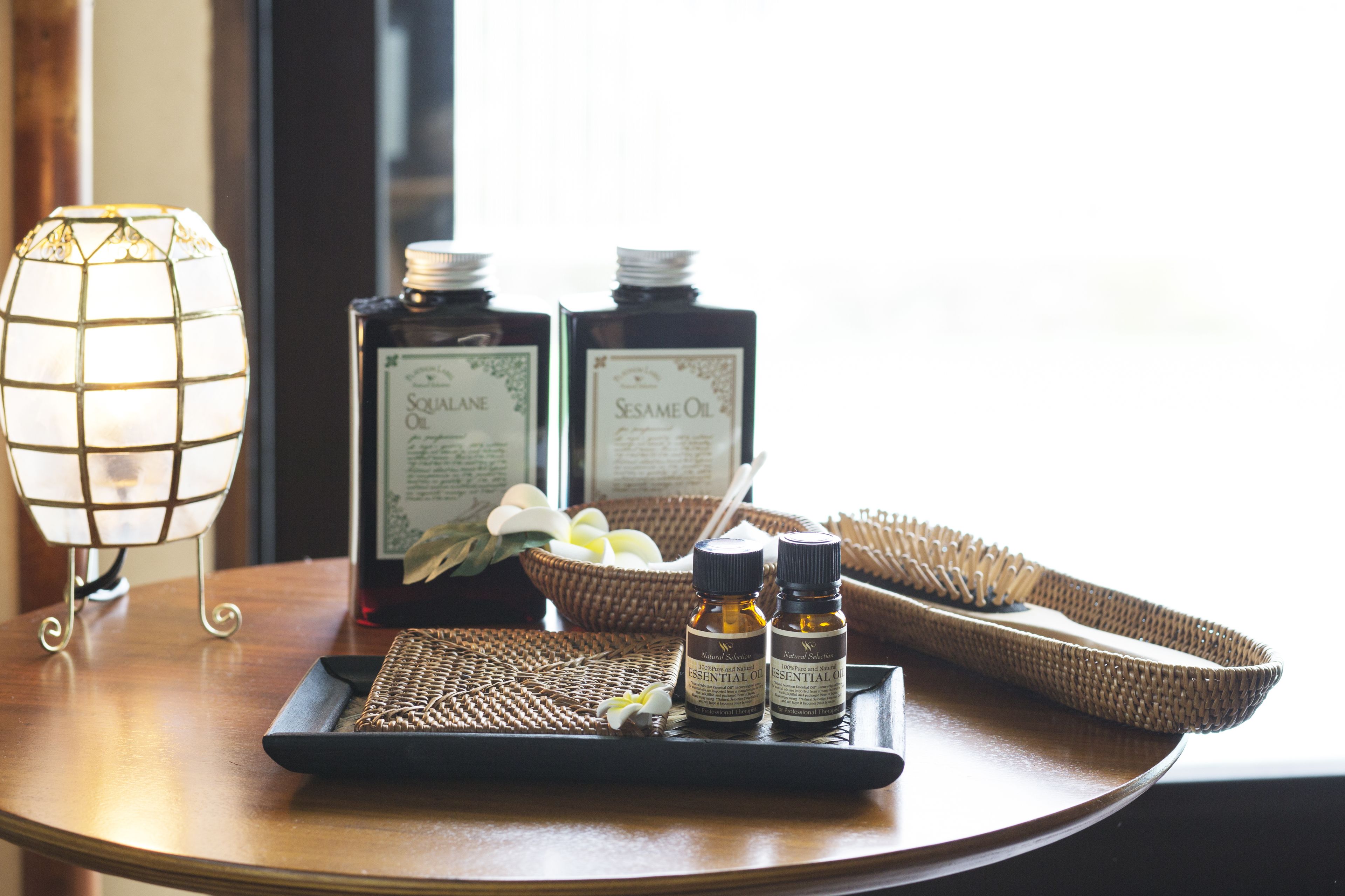 A tray with essential oils, a candle, and a woven basket on a wooden table.