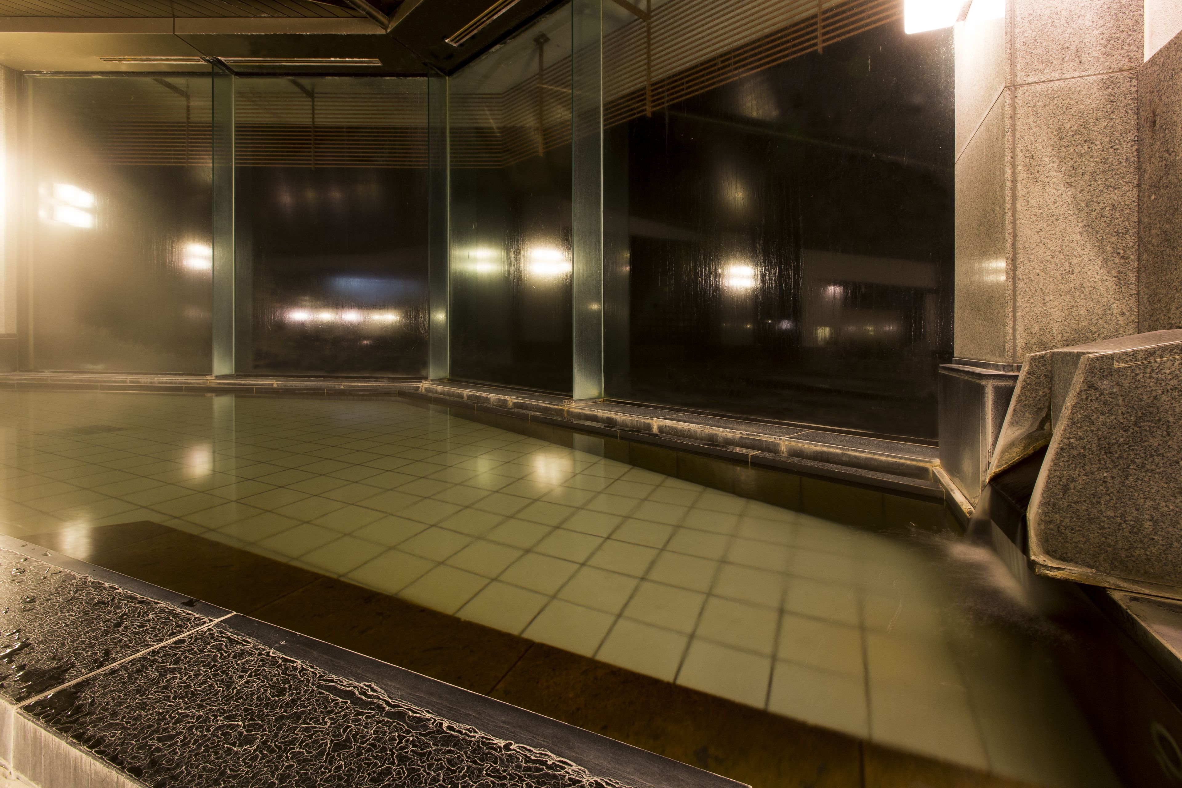 A subway station with tiled floors, glass walls, and a bench.
