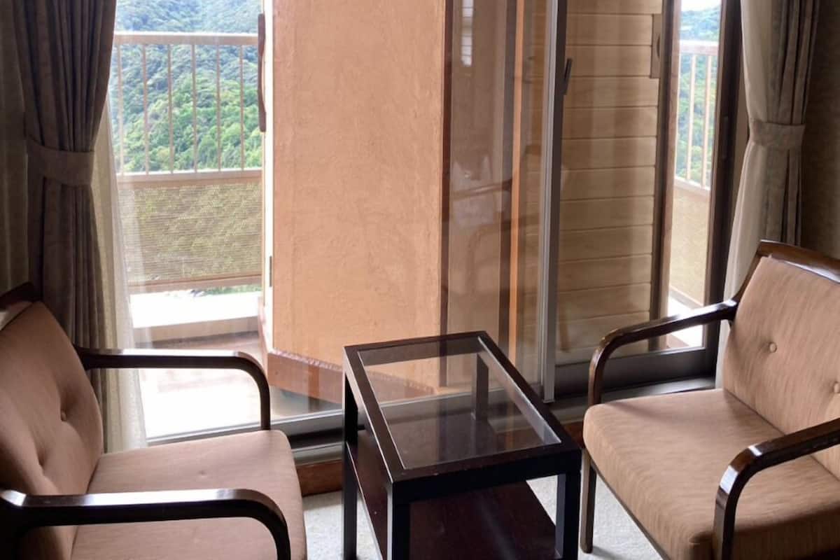 Un balcón con puerta de cristal, dos sillas, una mesita y vista a un paisaje montañoso.