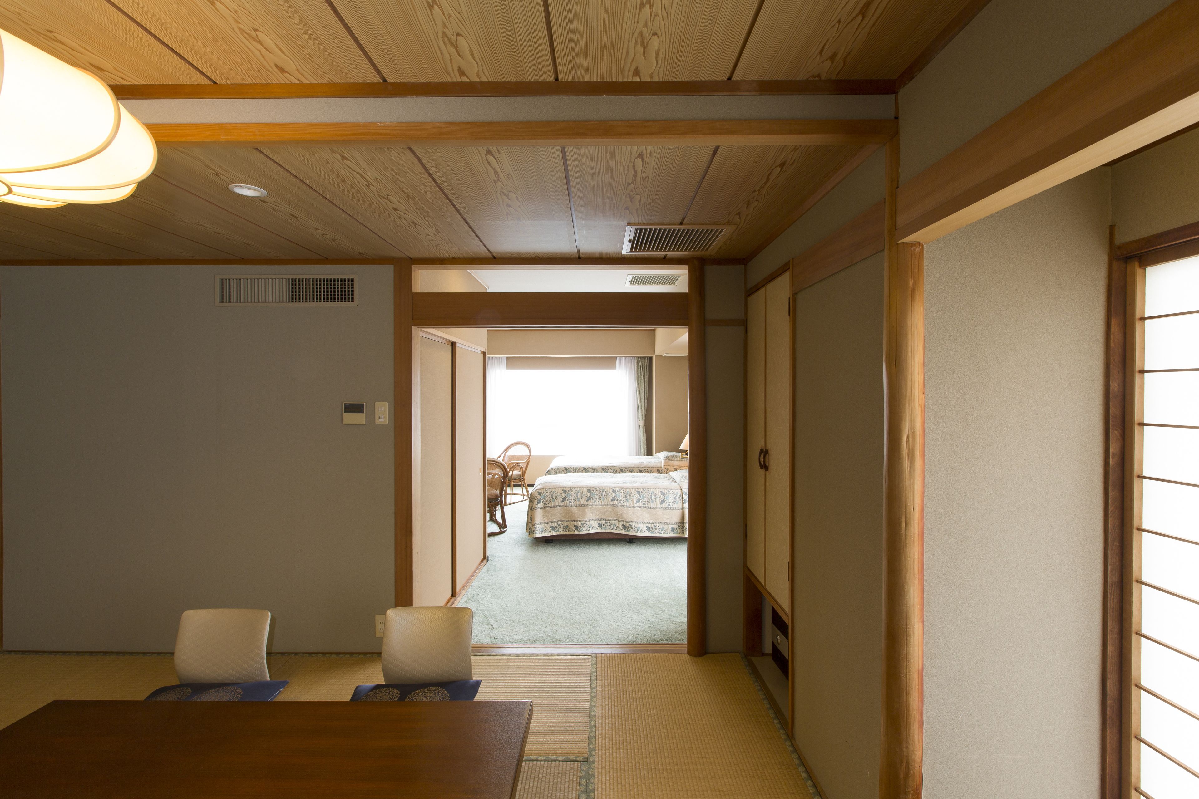 A traditional Japanese room with tatami flooring, a wooden table, and a bed with a patterned bedspread.