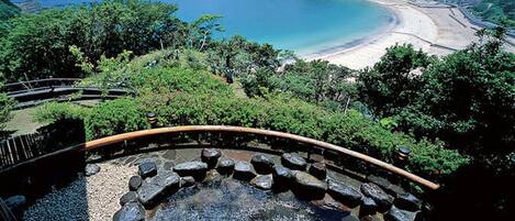 A hot spring surrounded by lush greenery and a beach in the background.