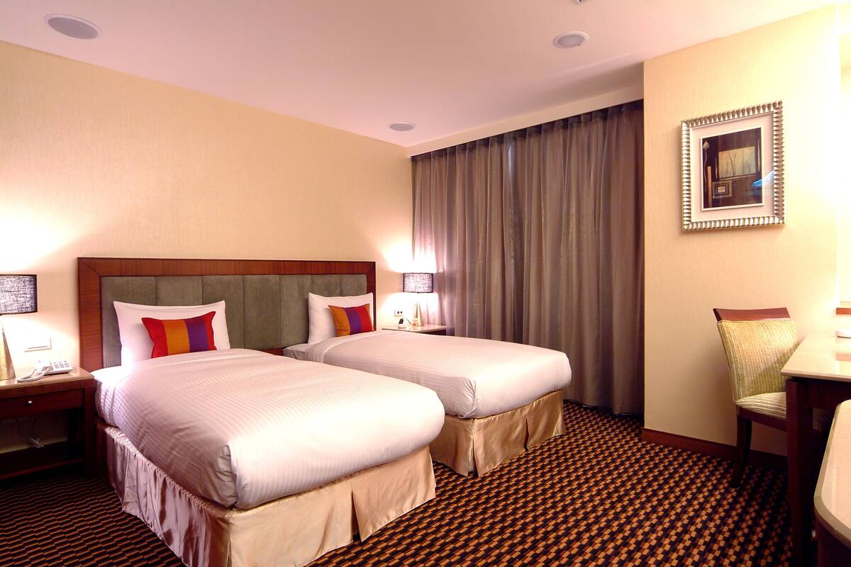A hotel room with two beds, a chair, a desk, and a patterned carpet.