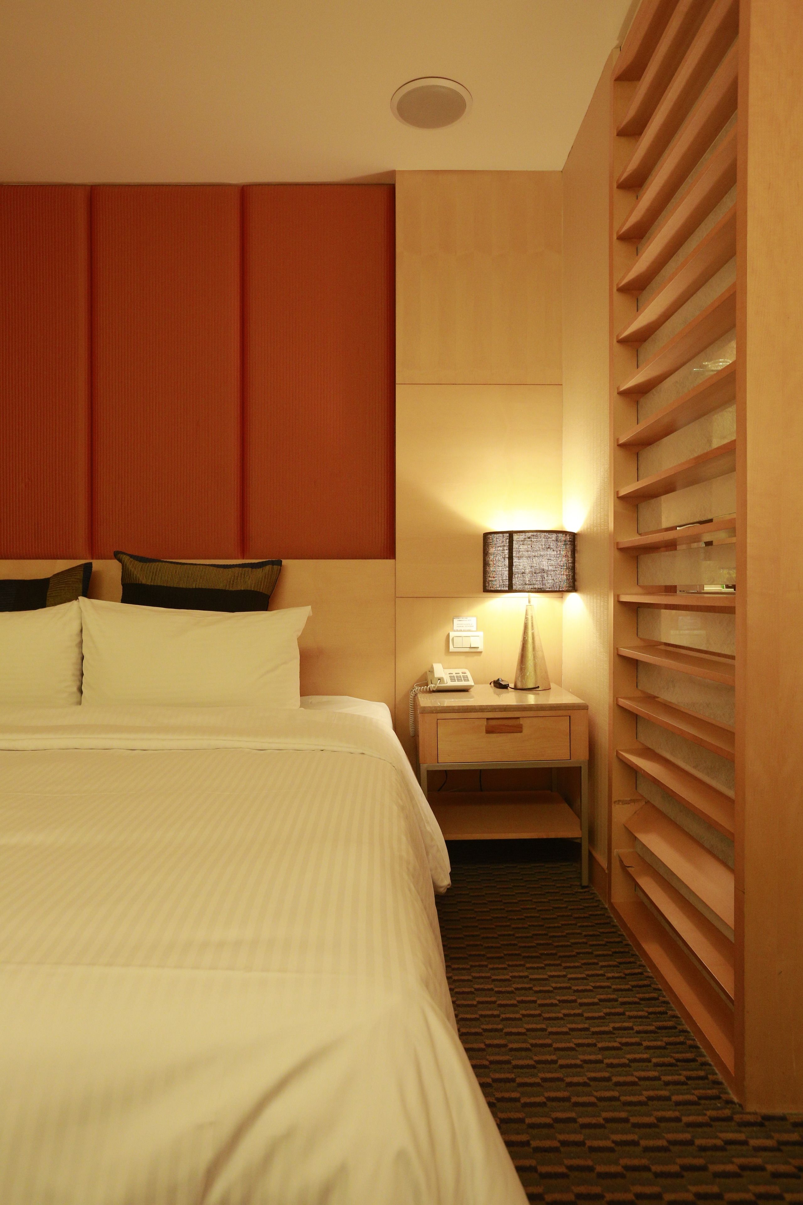 A hotel room with a large bed, a bedside table with a lamp, and a built-in shelving unit.