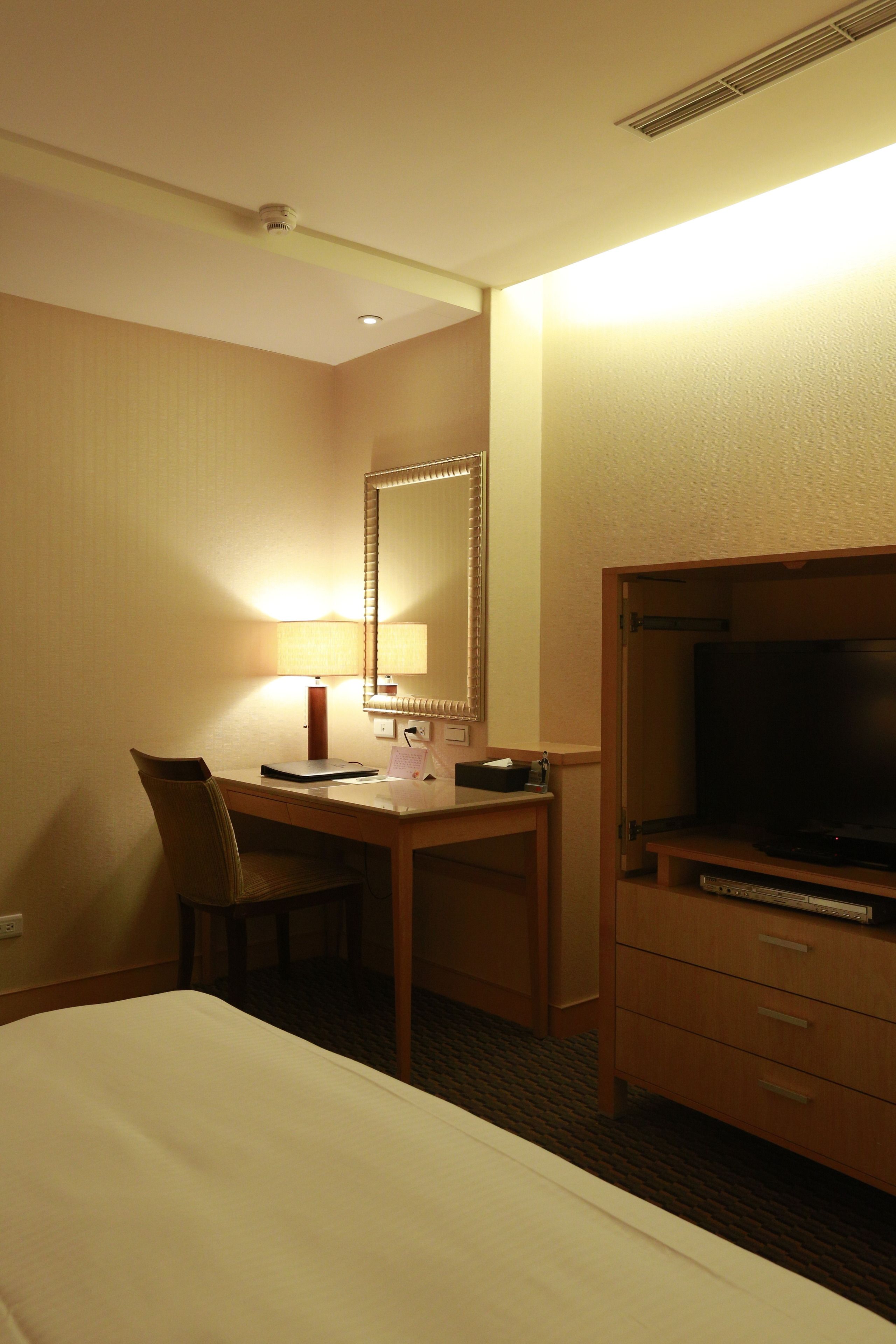 A hotel room with a bed, a desk with a chair, a television, and a mirror.
